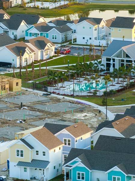 New residential development with colorful houses, a pool, and construction sites, near a lake.