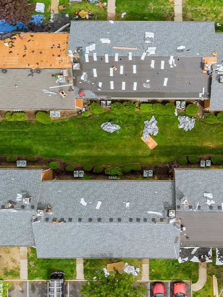 Aerial view of rooftops, some damaged, with debris on grass below.