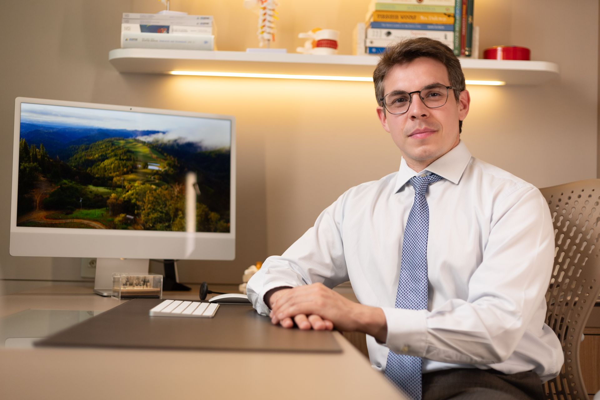 Um homem está sentado em uma mesa segurando um modelo de coluna vertebral.