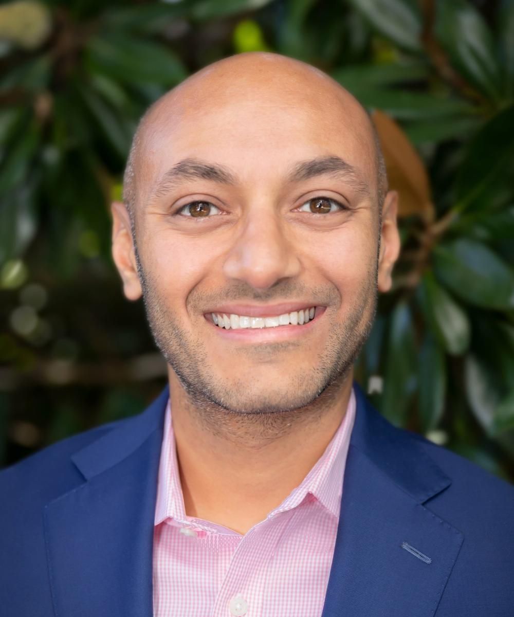 A bald man in a blue suit and pink shirt is smiling for the camera.