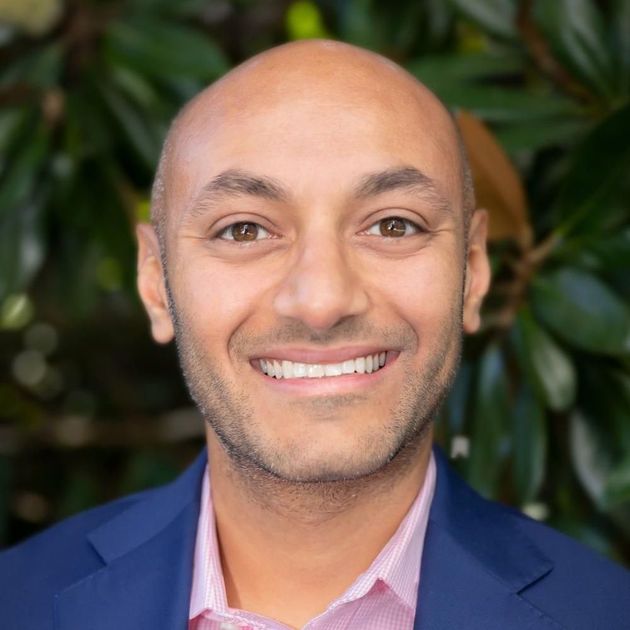 A bald man in a blue suit and pink shirt is smiling for the camera.