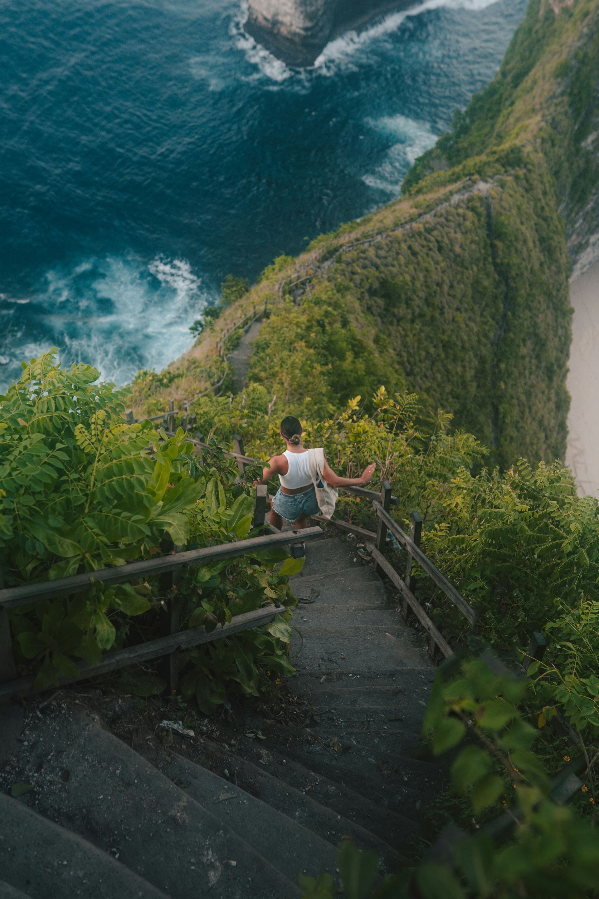 A man is sitting on a set of stairs on a cliff overlooking the ocean.