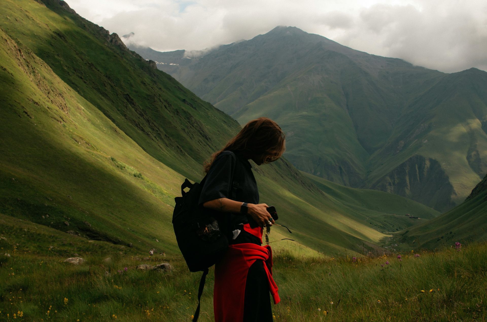 A woman with a backpack is standing in front of a mountain.