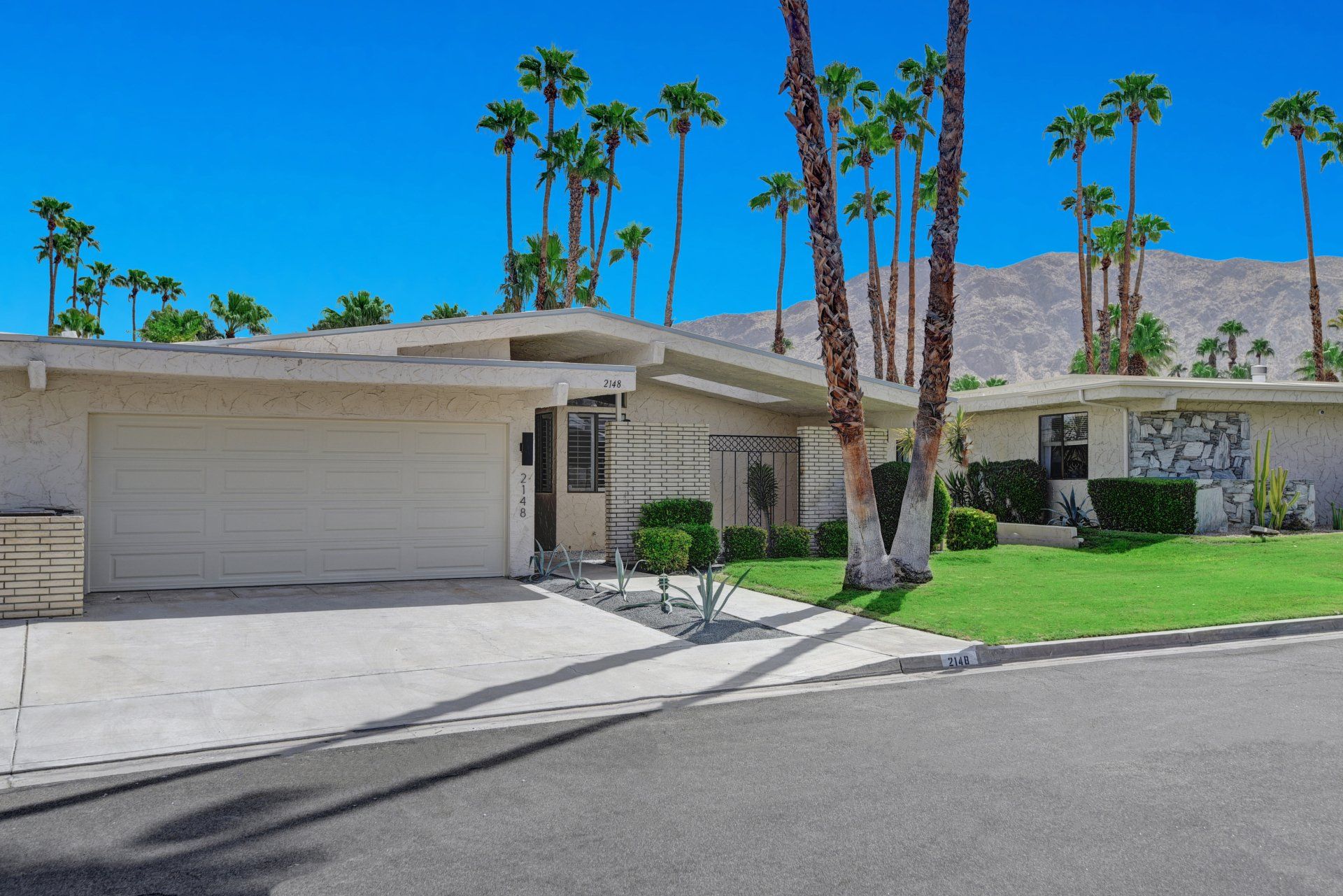 A white house with palm trees in front of it and mountains in the background.