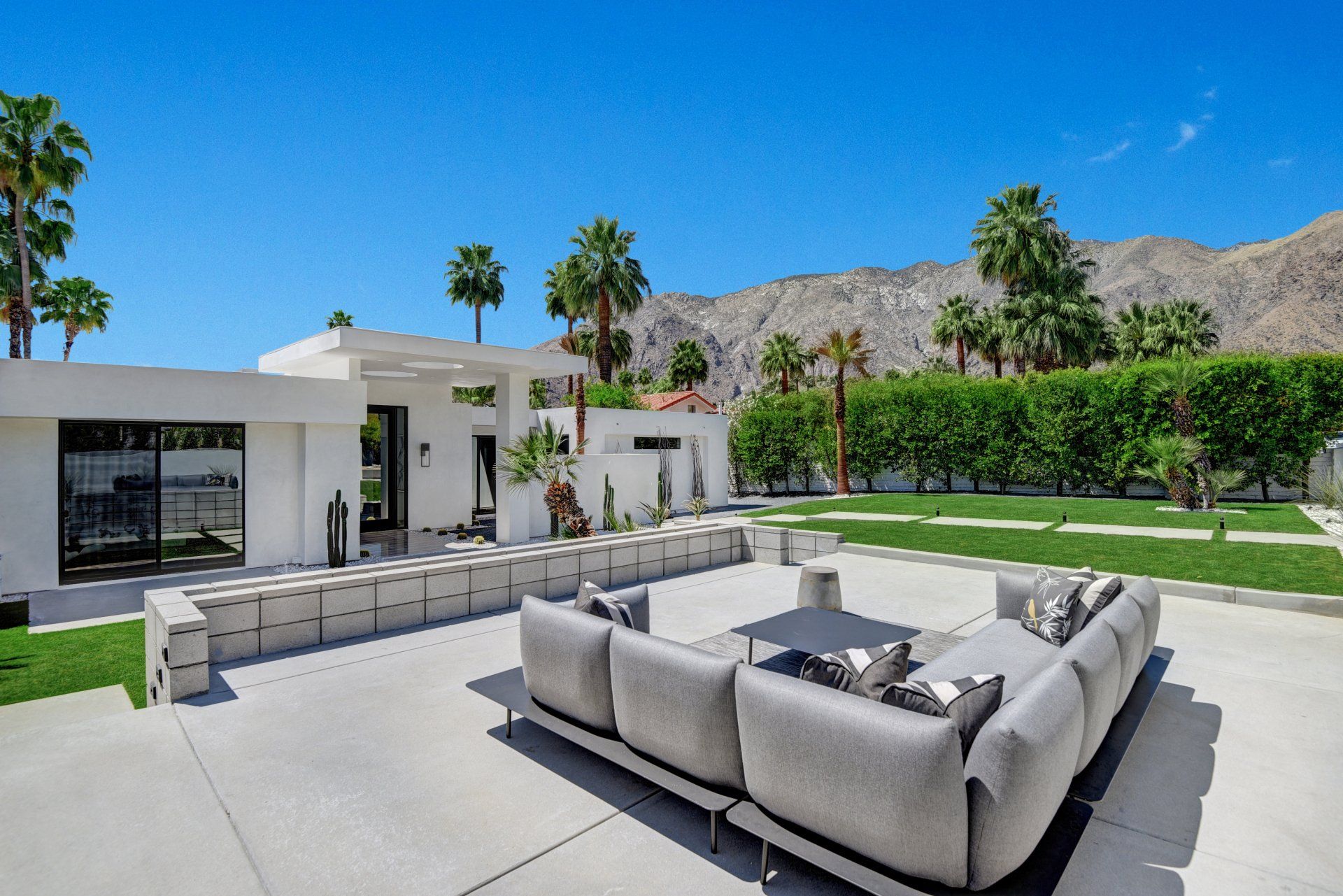 A large couch is sitting on a patio in front of a white house.