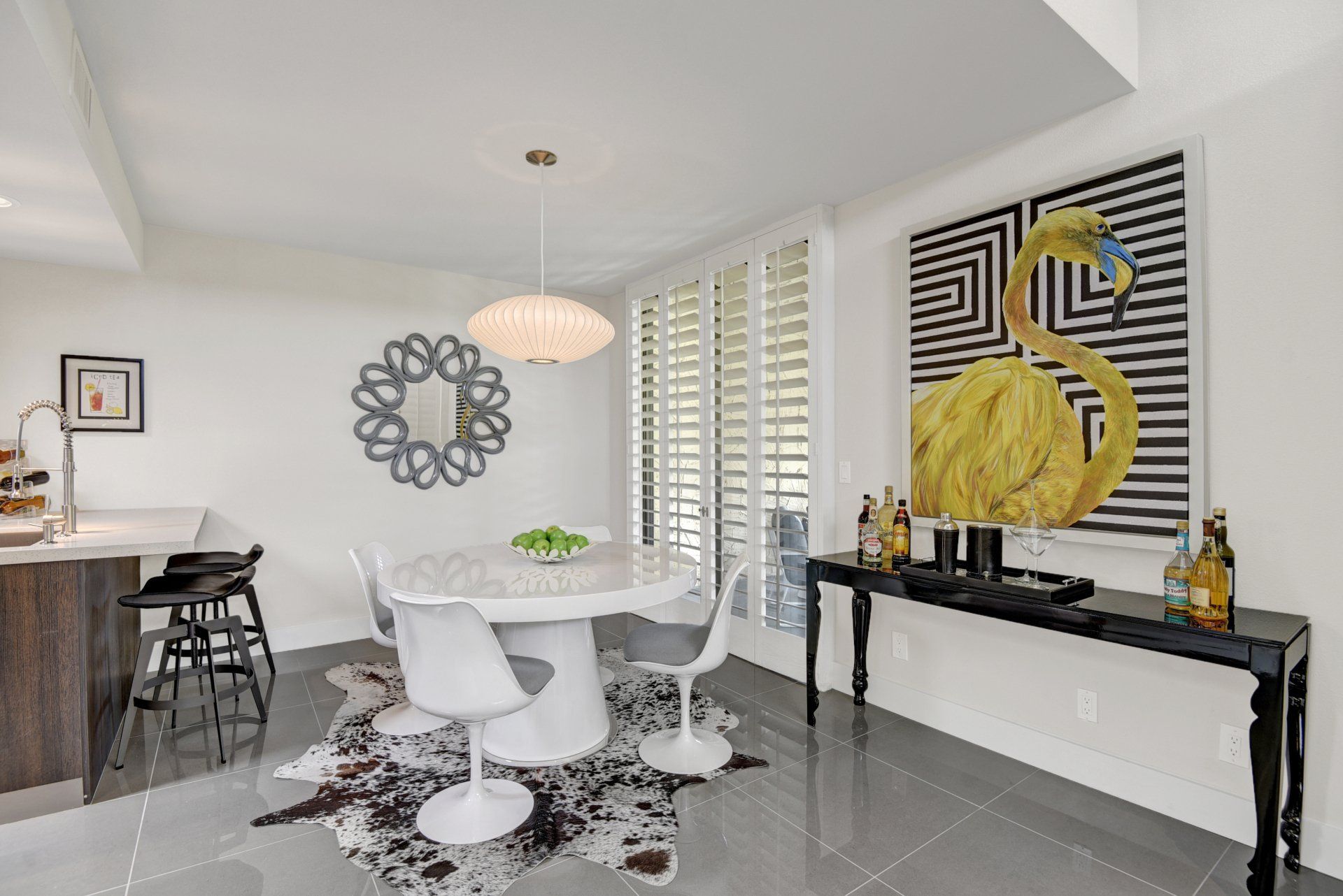 A dining room with a table and chairs and a painting of a flamingo on the wall.