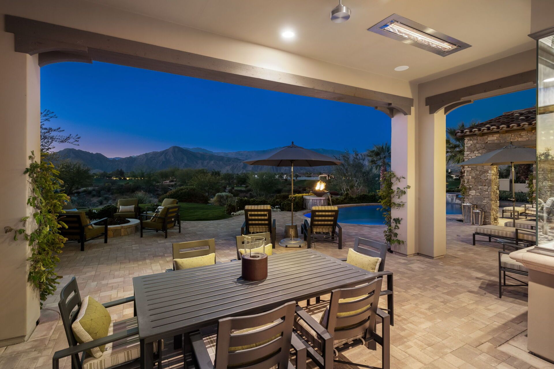 A patio with a table and chairs and a pool at night.