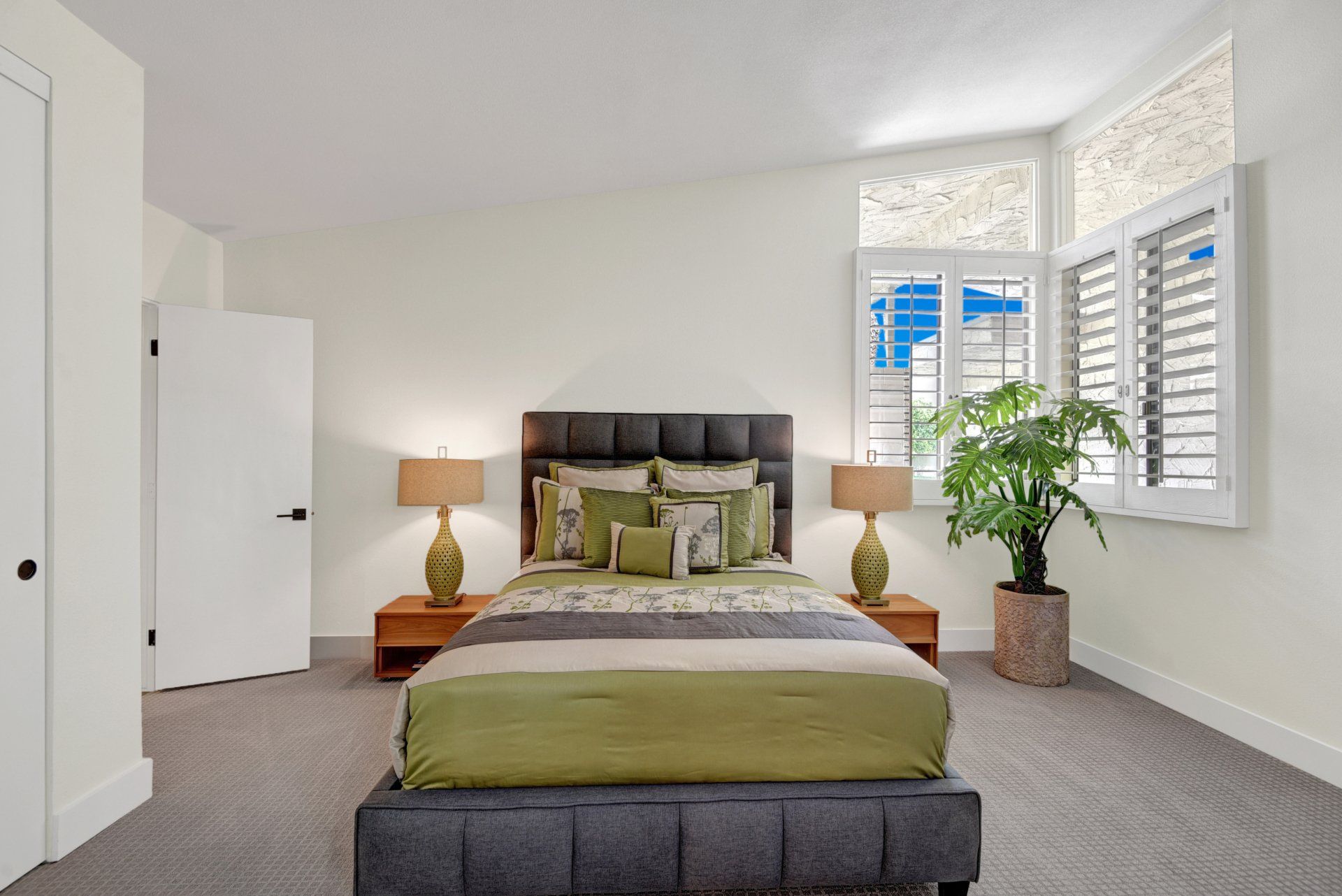 A bedroom with a bed , lamps , a plant and a window.