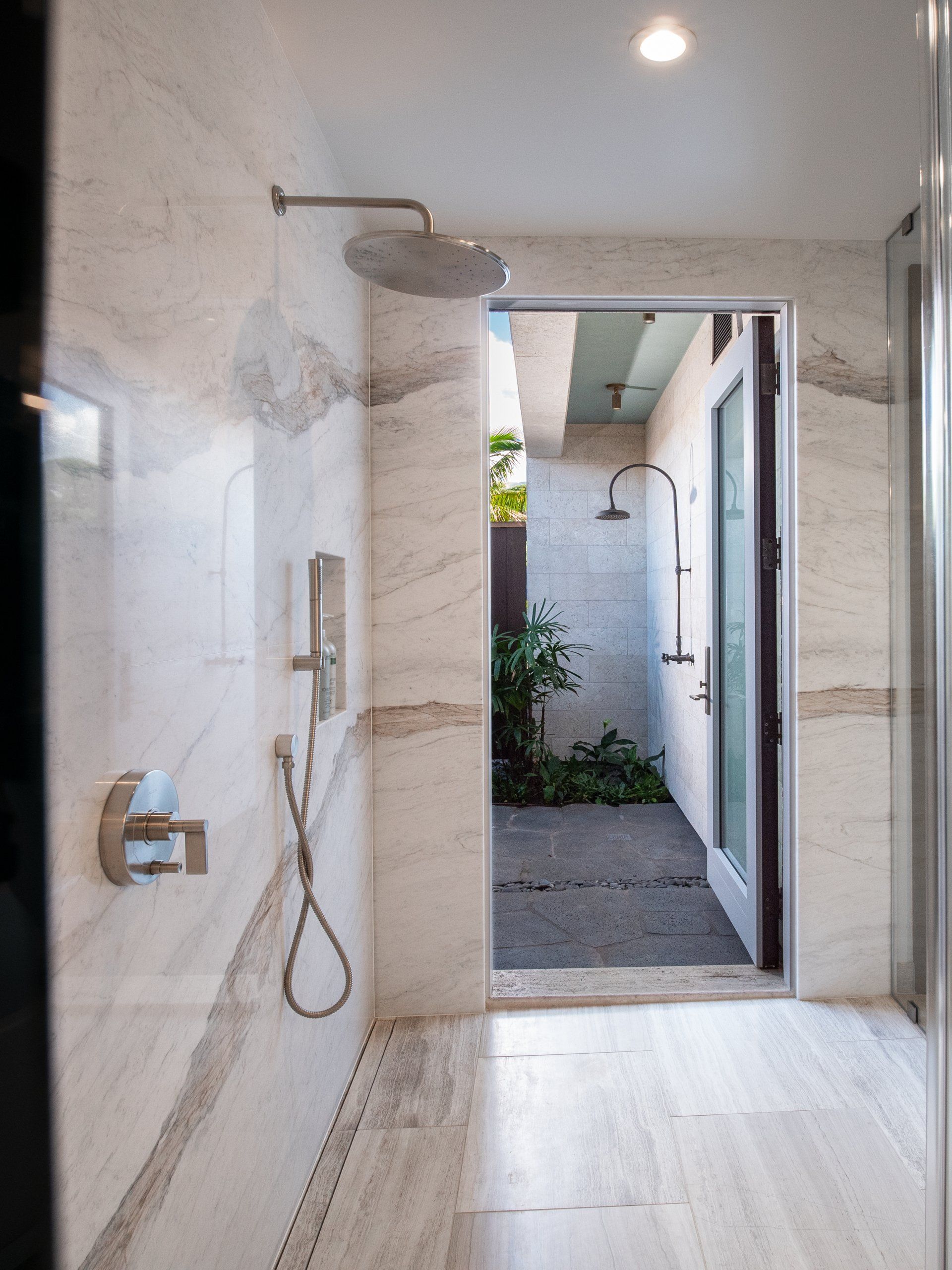 A bathroom with a walk in shower and a door leading to a outside shower.