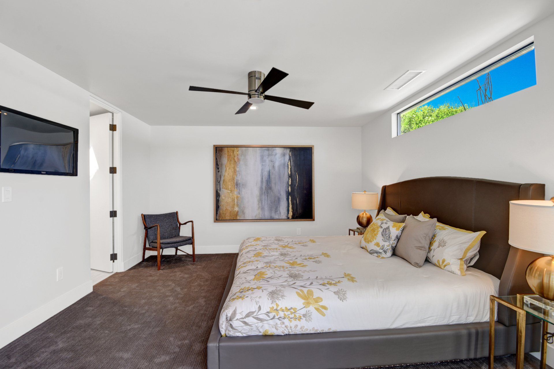 A bedroom with a large bed , a chair , a television and a ceiling fan.