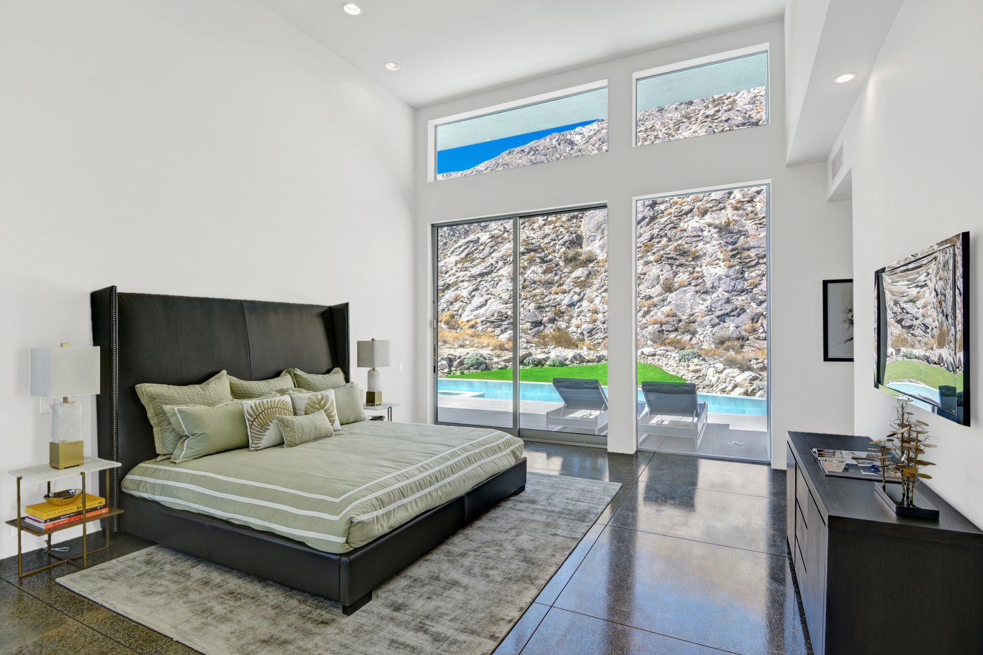 A bedroom with a large bed , dresser , television and sliding glass doors leading to a pool.