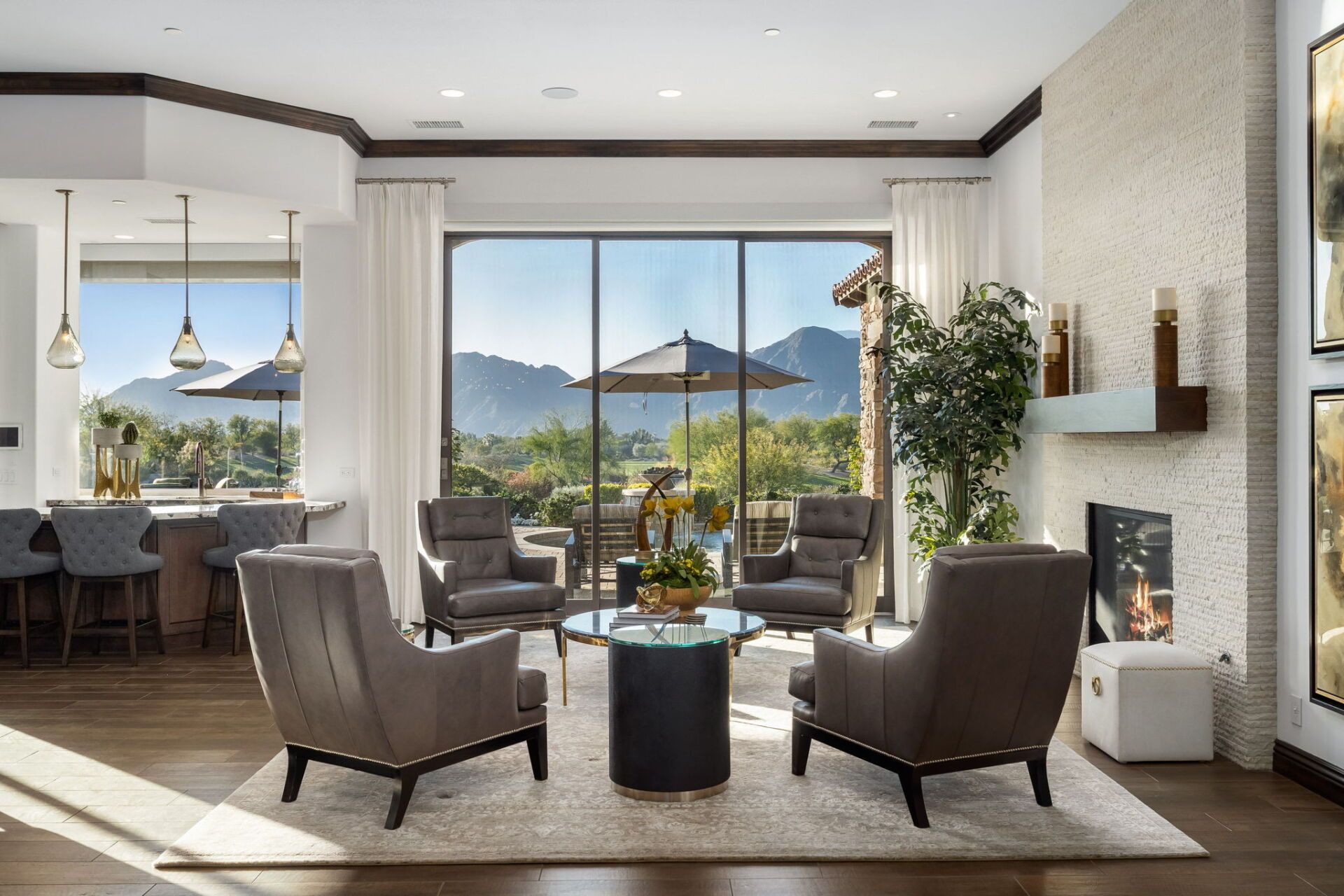 A living room with a fireplace , chairs , a table and a view of the mountains.