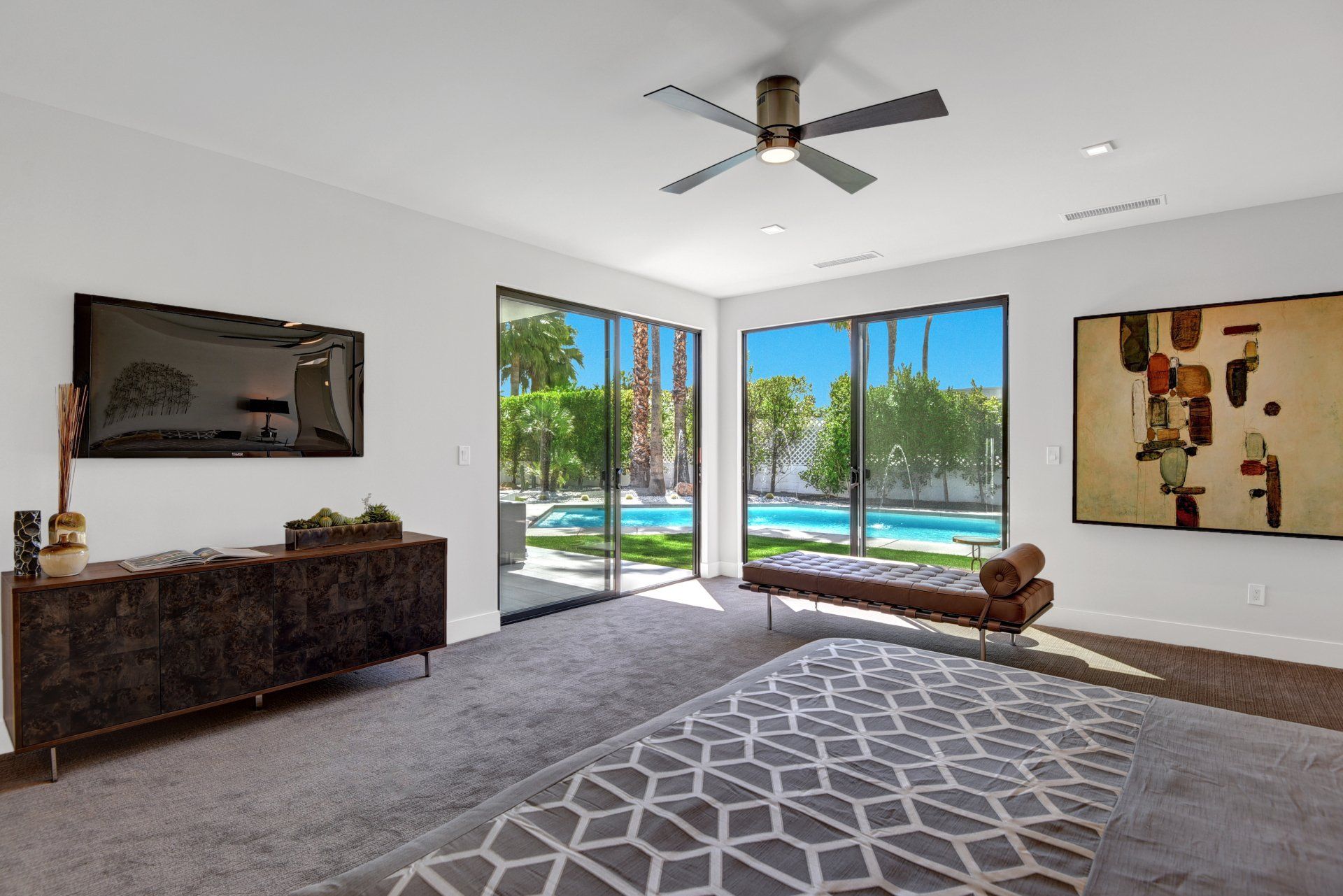 A living room with a ceiling fan , sliding glass doors , a rug and a television.