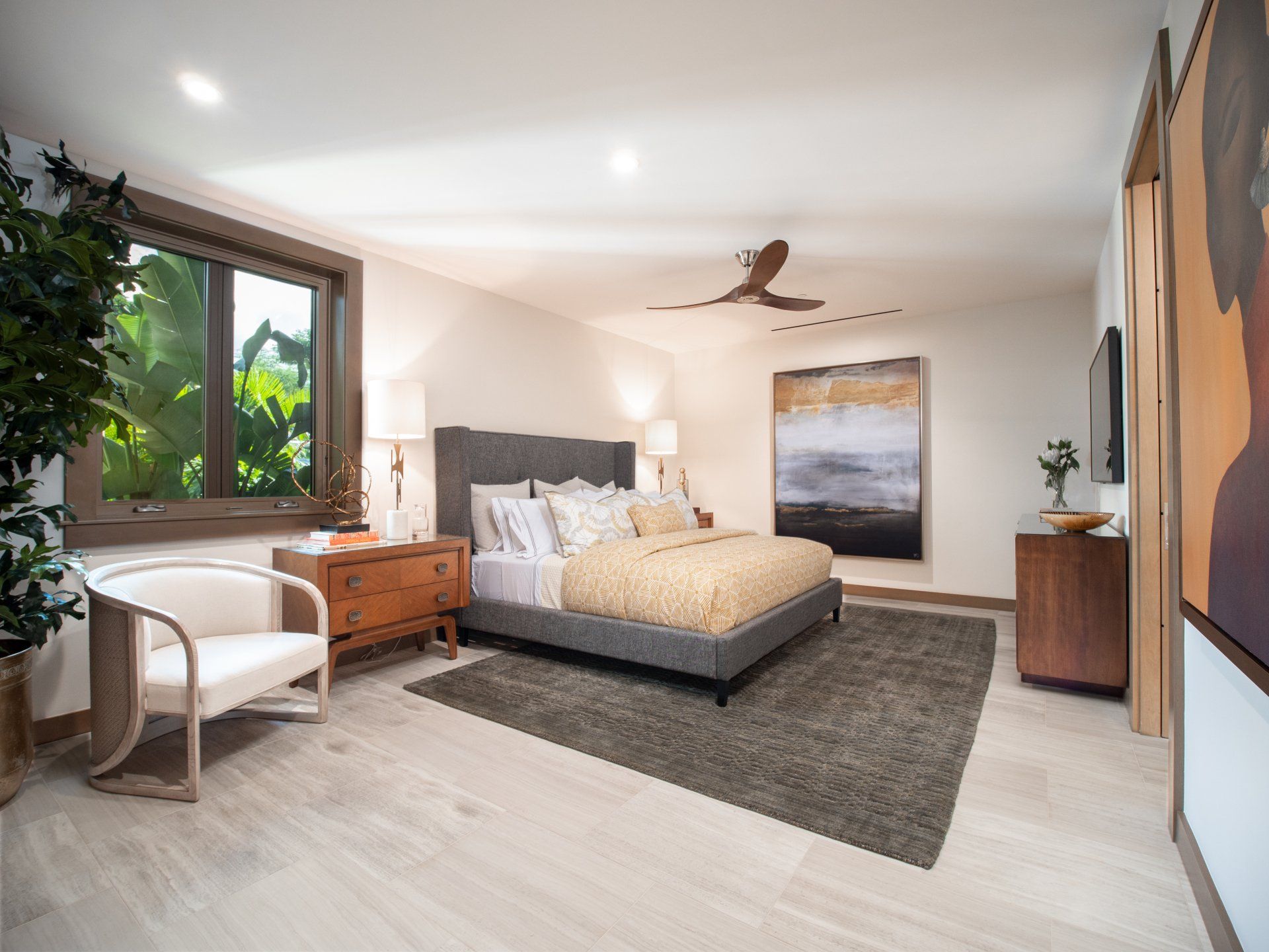 A bedroom with a large bed , chair , nightstand , rug and ceiling fan.