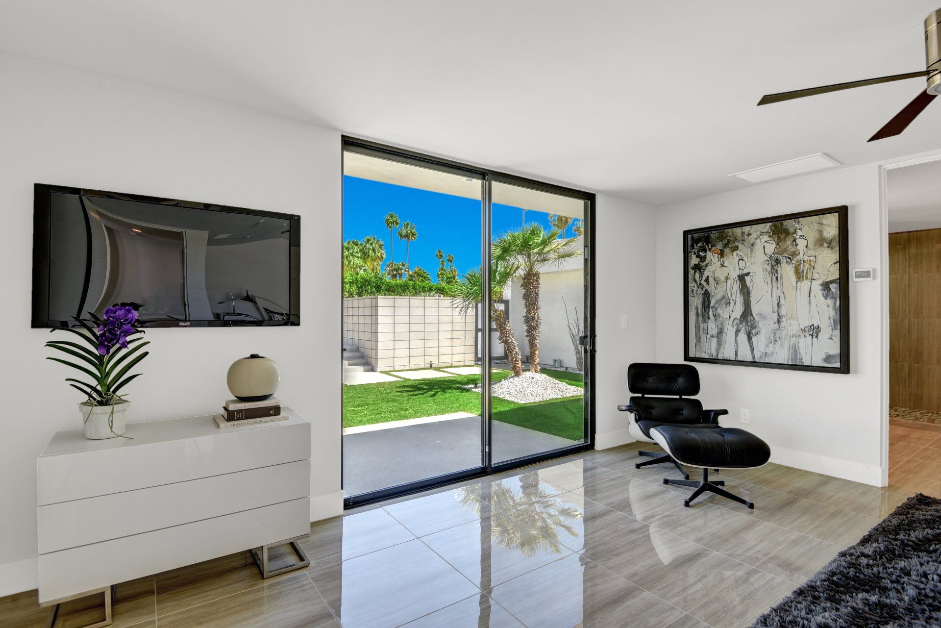 A living room with a sliding glass door , a chair , a television and a ceiling fan.