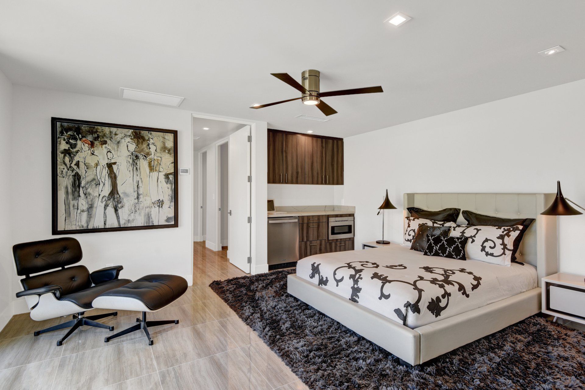 A bedroom with a large bed , chair , rug and ceiling fan.