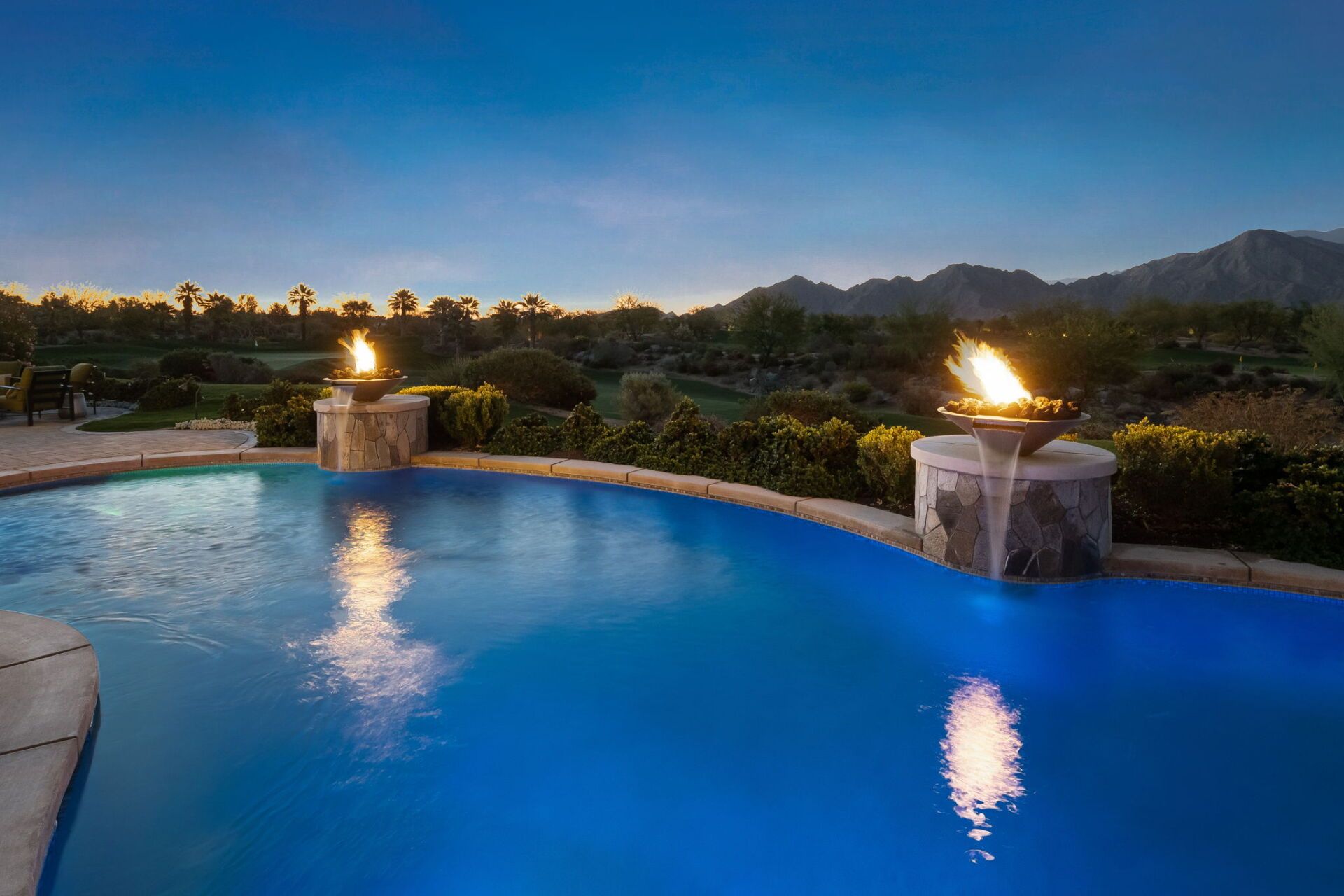A large swimming pool with two fire pits in the middle of it at night.