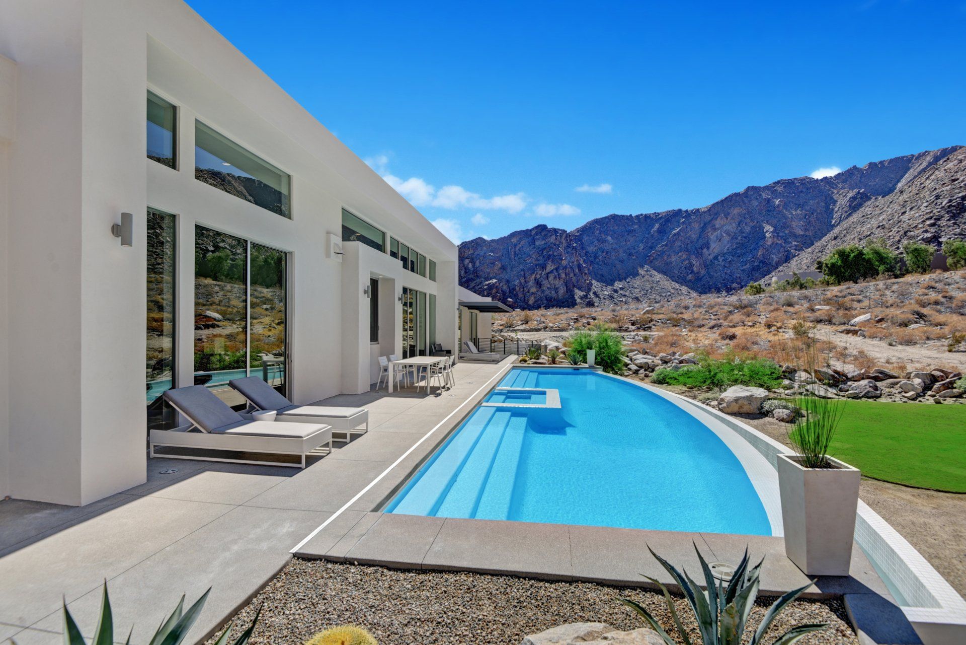 A large swimming pool in front of a house with mountains in the background