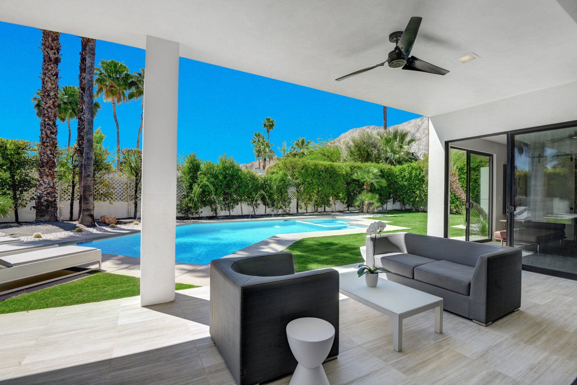 A patio with a couch and chairs and a ceiling fan overlooking a pool.