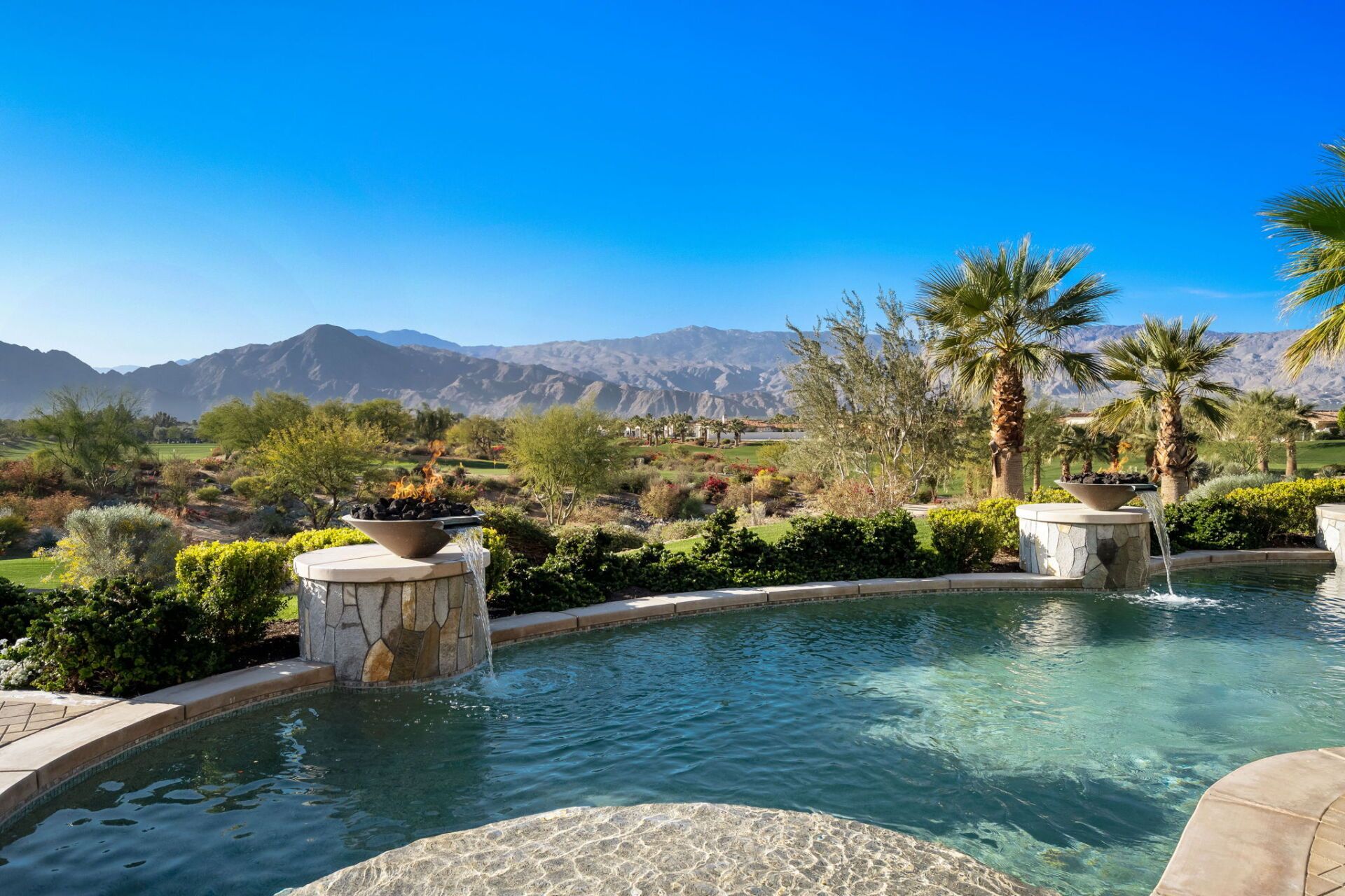 A large swimming pool with a fountain and mountains in the background.