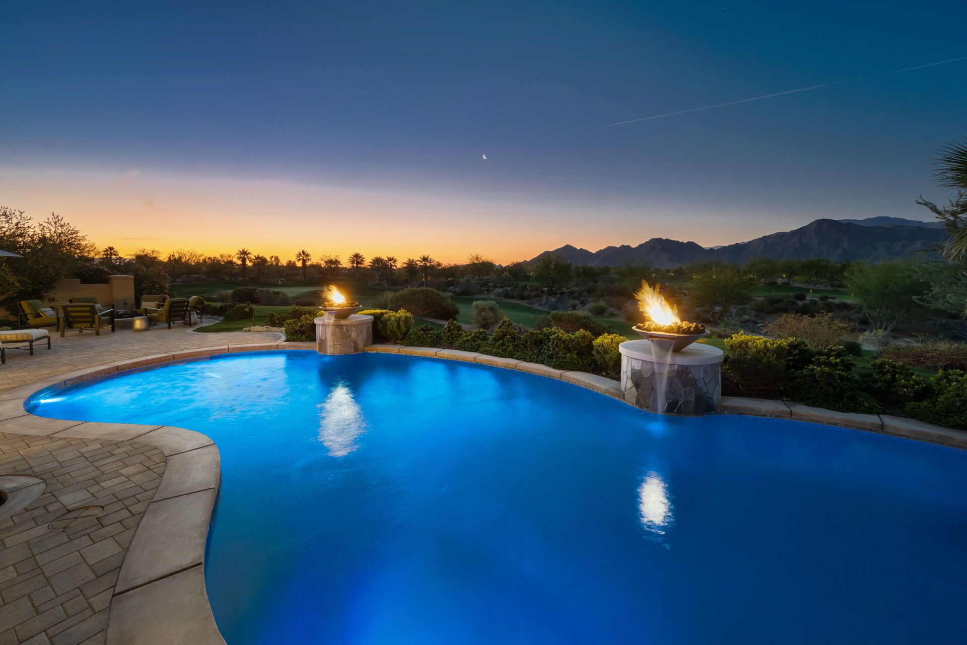 A large swimming pool is lit up at night with mountains in the background.