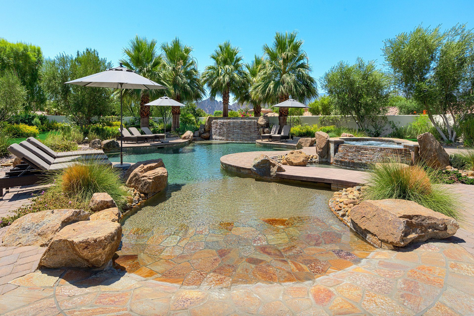 A large swimming pool surrounded by rocks and palm trees on a sunny day.