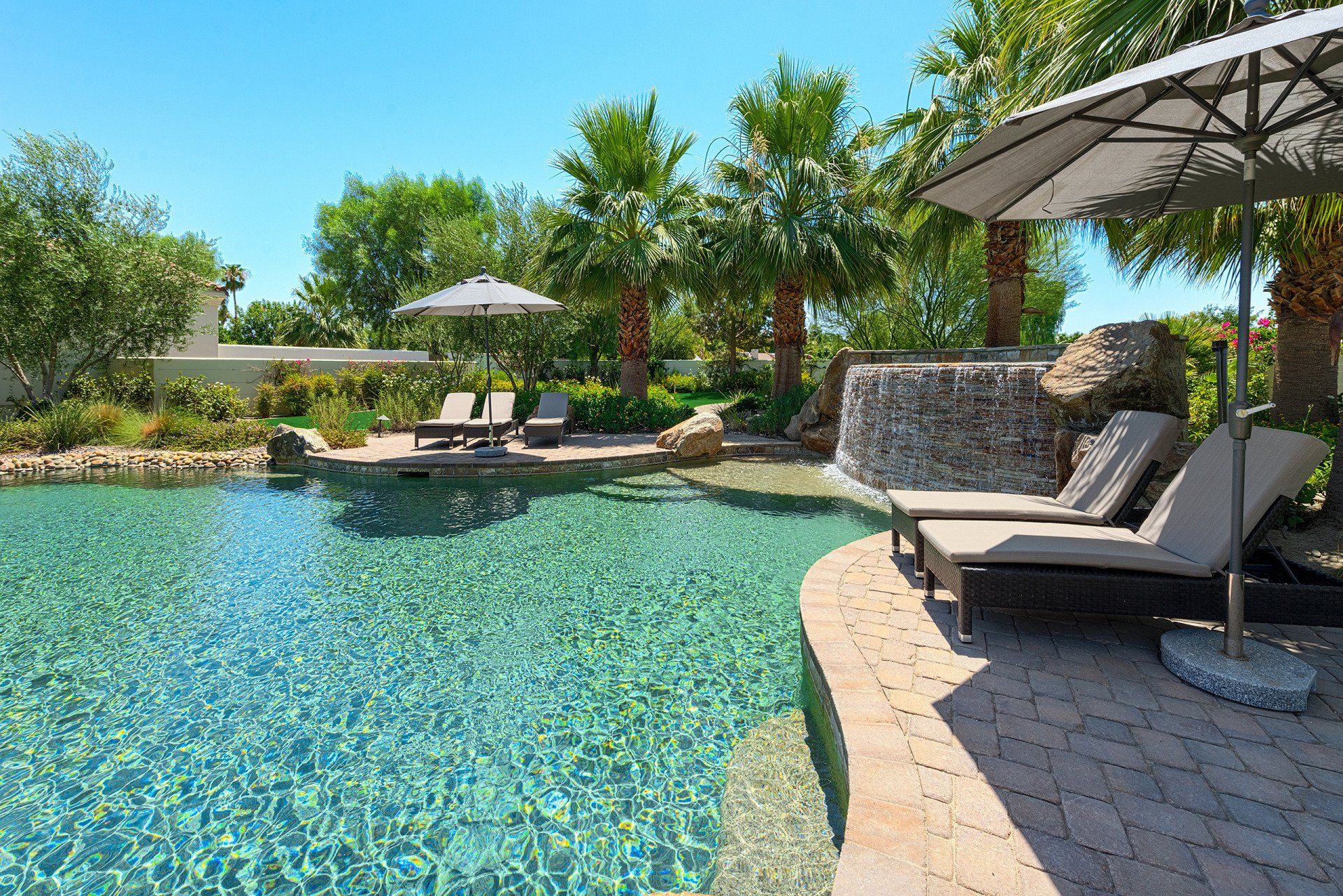 A large swimming pool surrounded by chairs and umbrellas on a sunny day.