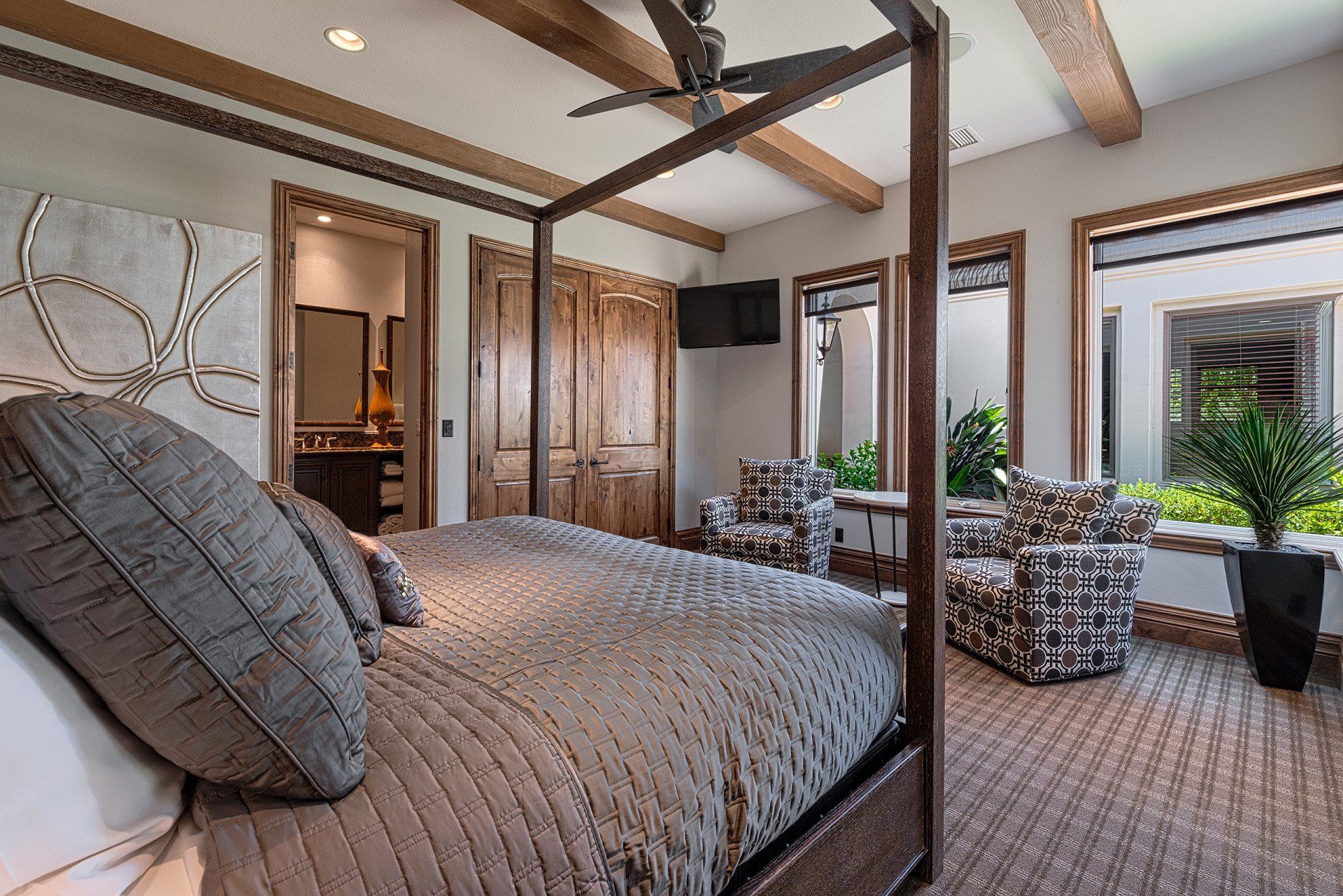 A bedroom with a four poster bed , chairs and a ceiling fan.