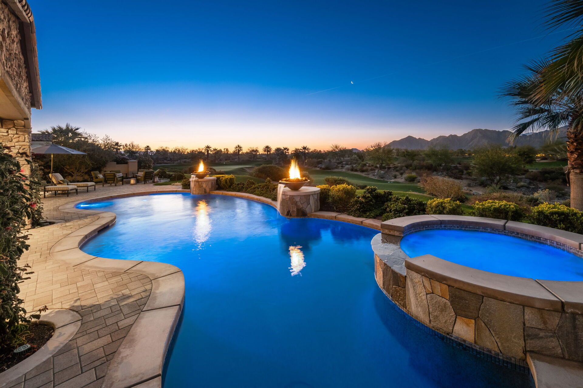 A large swimming pool with a hot tub in the backyard at night.