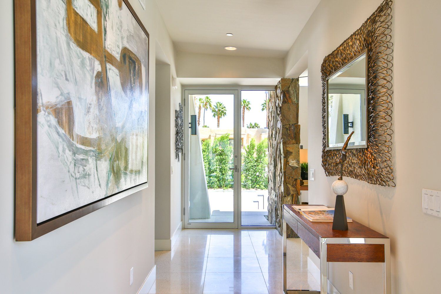 A hallway with a table , mirror and painting on the wall.