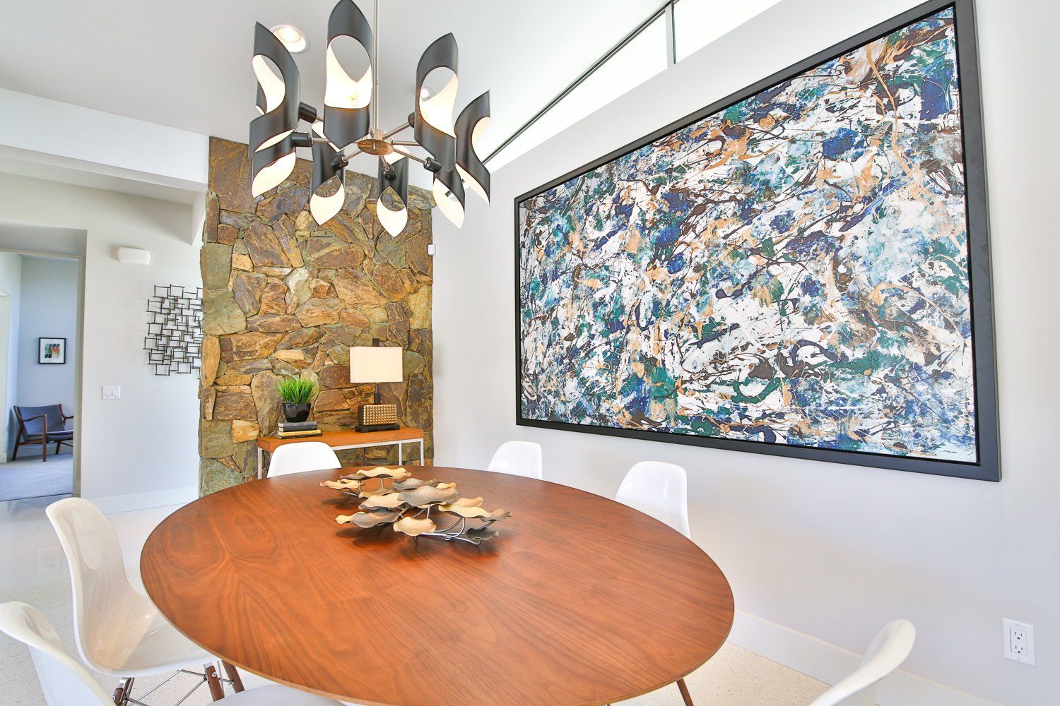A dining room with a round table and chairs and a large painting on the wall.