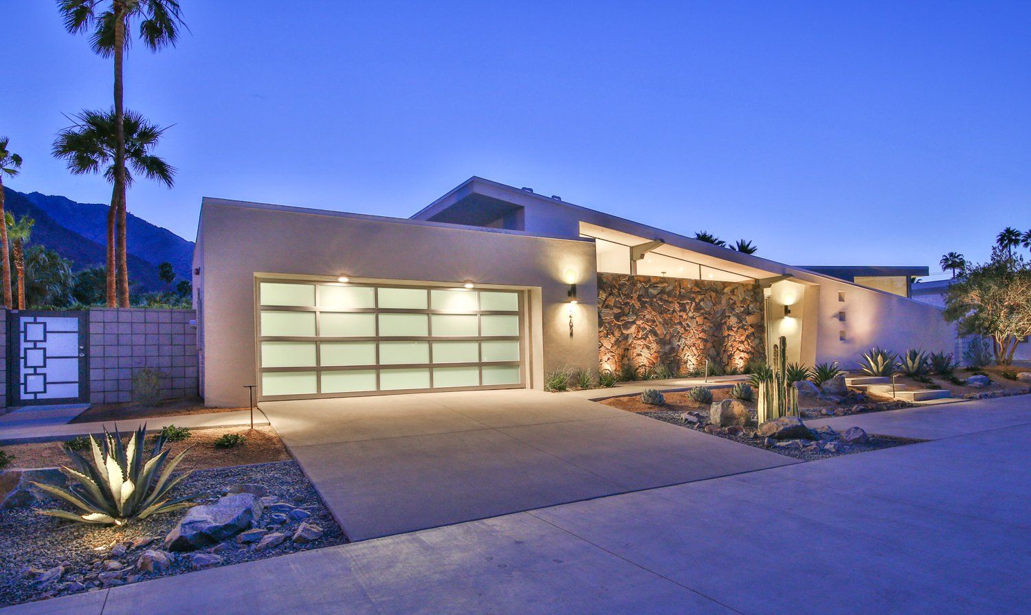 A modern house with a glass garage door is lit up at night.