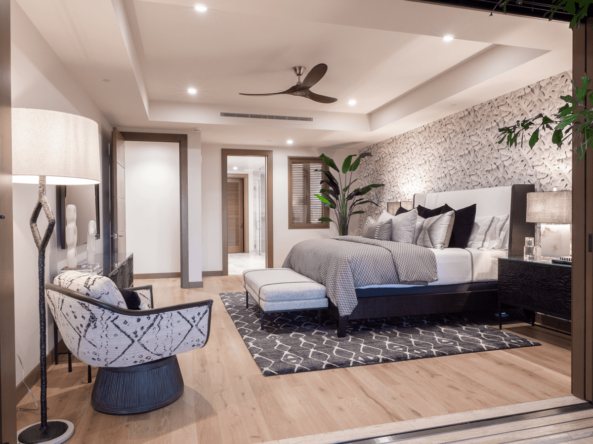 A bedroom with a large bed , chair , lamp and ceiling fan.