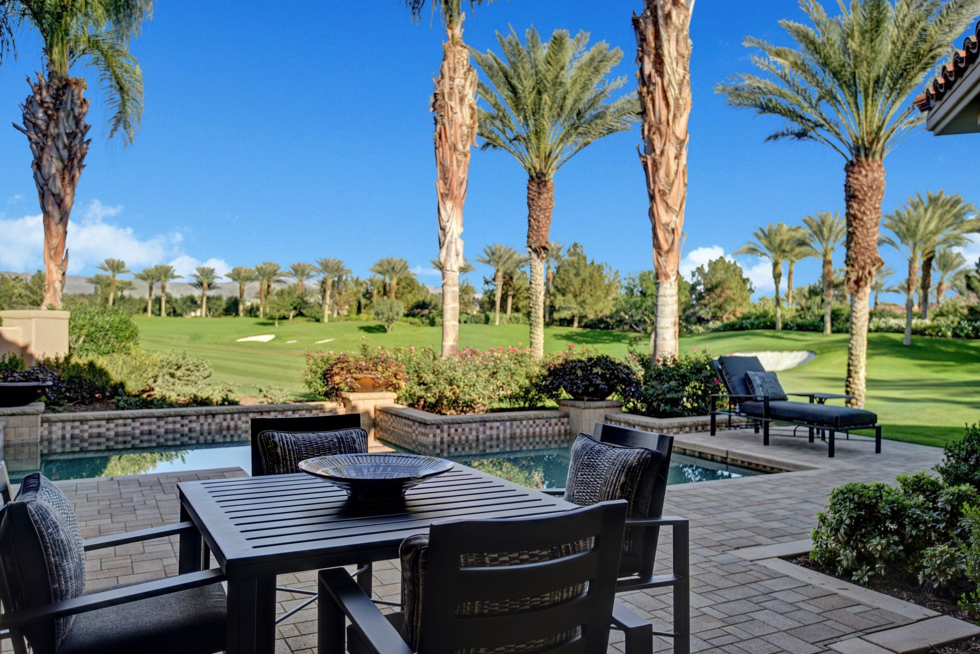 A patio with a table and chairs next to a pool and palm trees