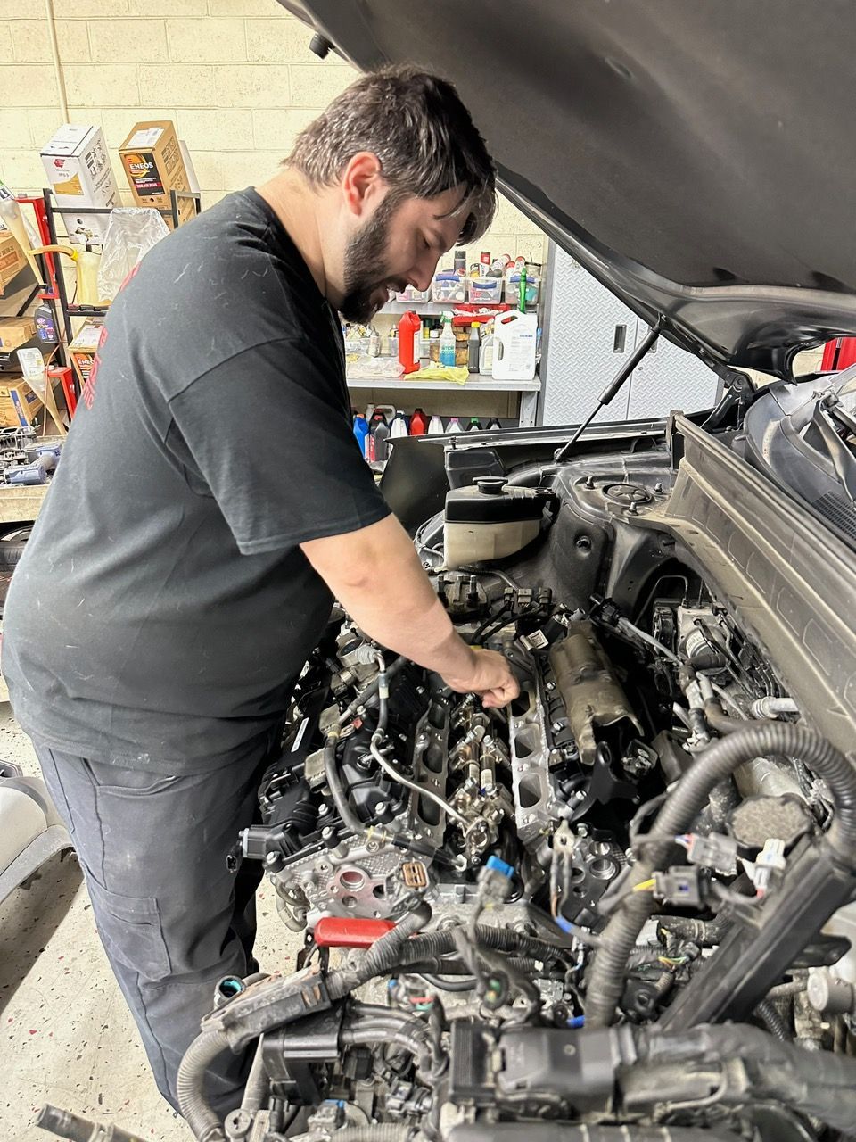 Two mechanics examine a car's undercarriage in a repair shop. One holds a clipboard; the other works on the vehicle.