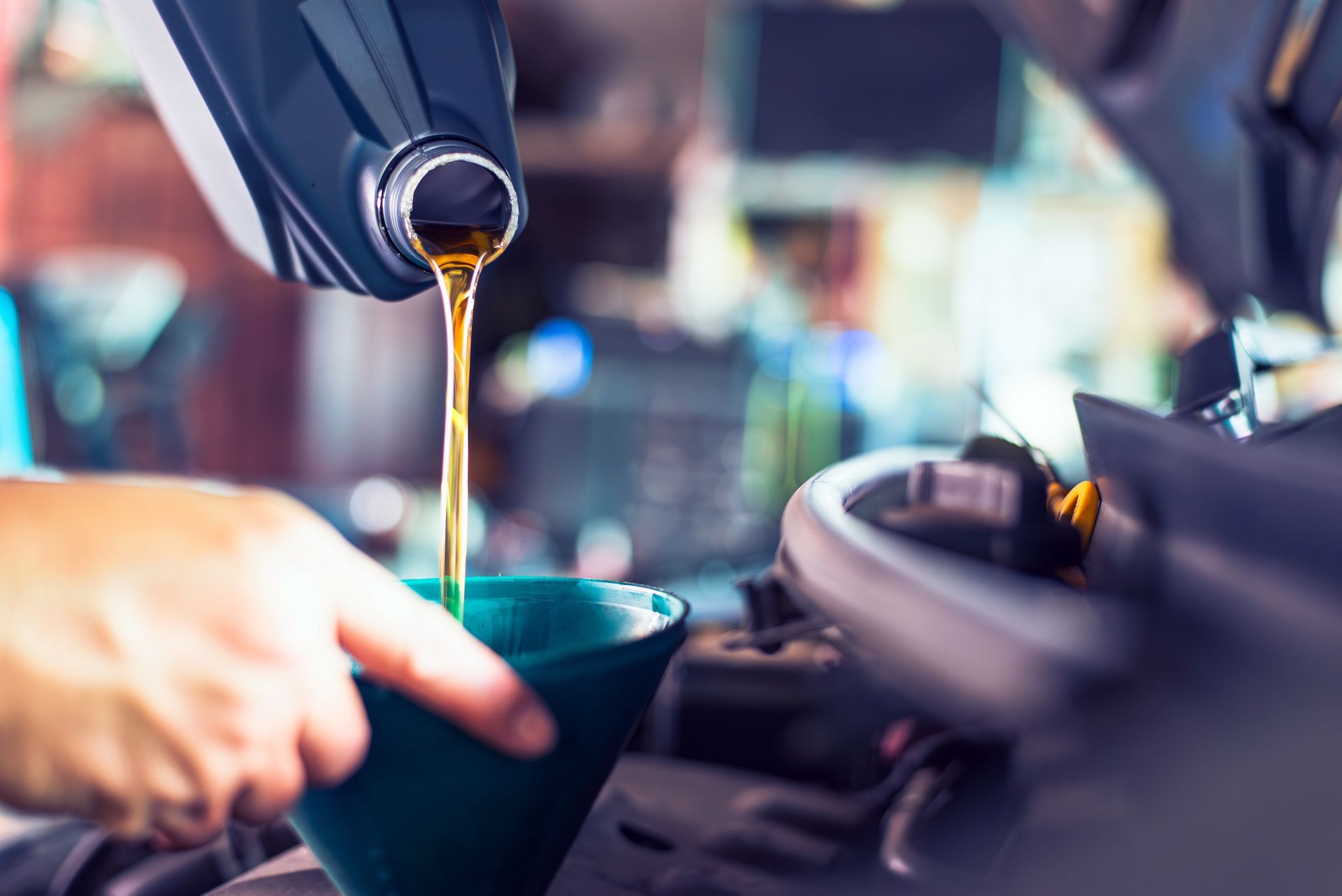Engine oil being poured from a plastic container through a green funnel into a car engine.
