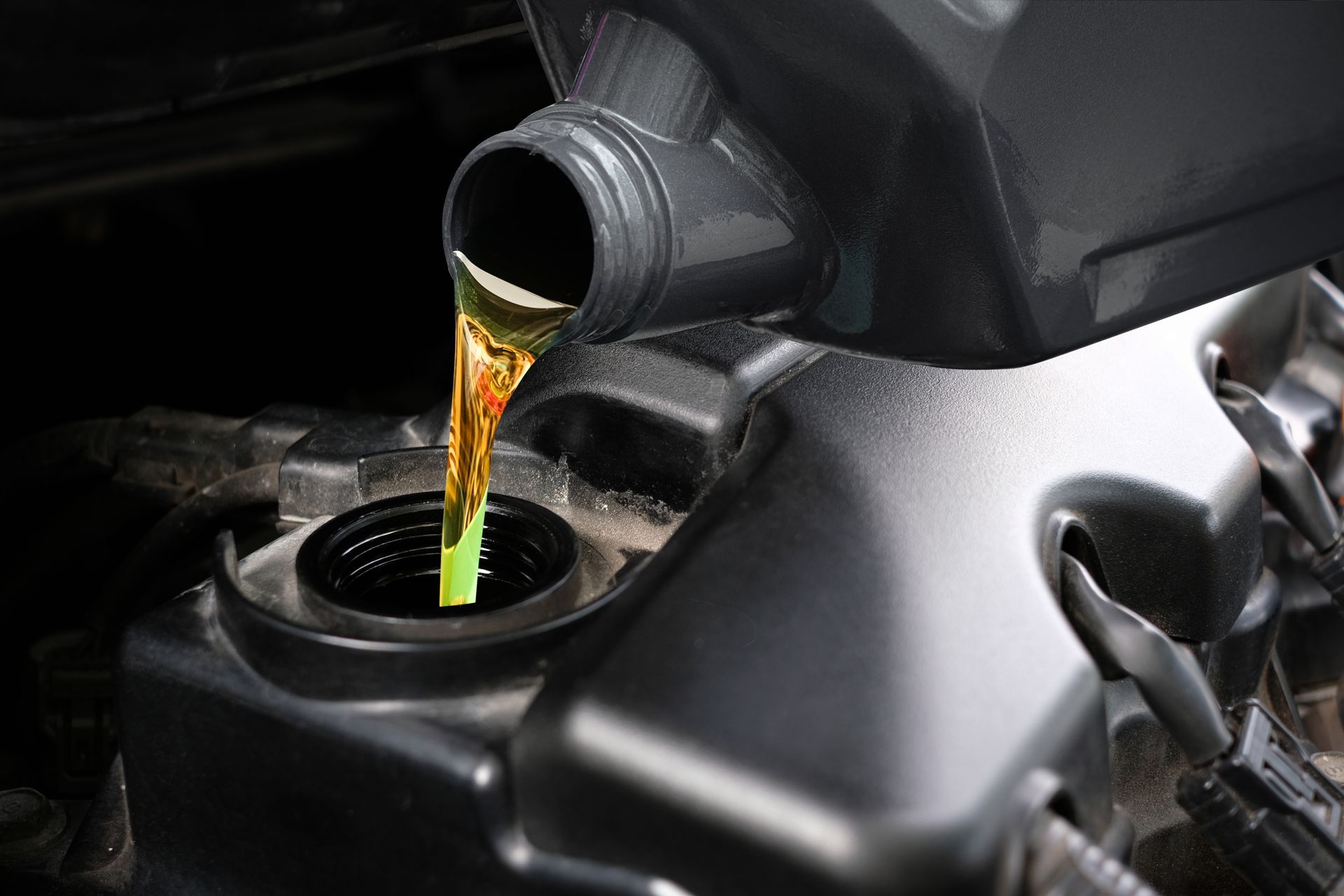 Pouring oil from a container into a car engine, yellow liquid.