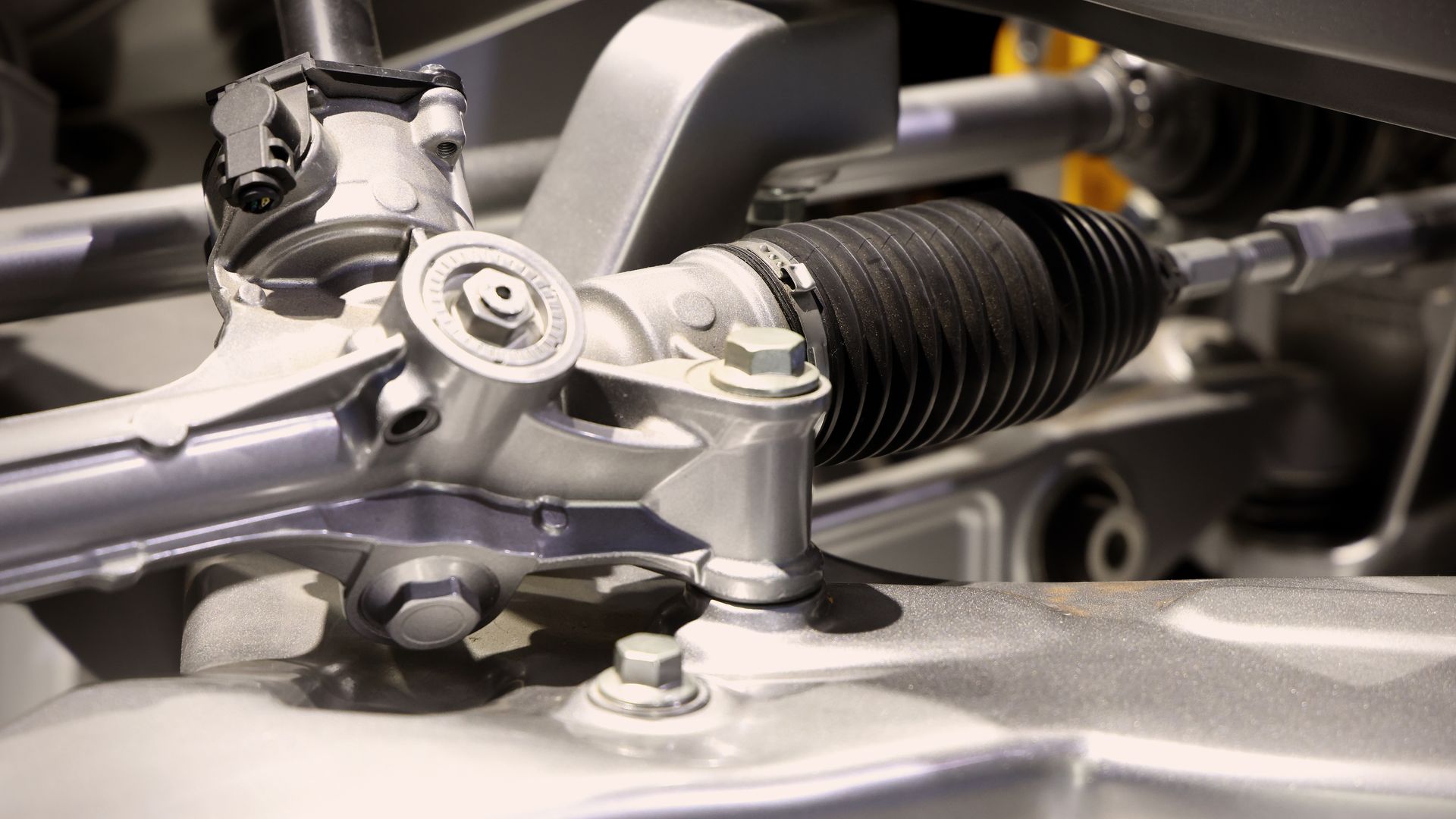 Close-up view of a metal car steering rack and pinion mechanism with a black rubber bellows boot.