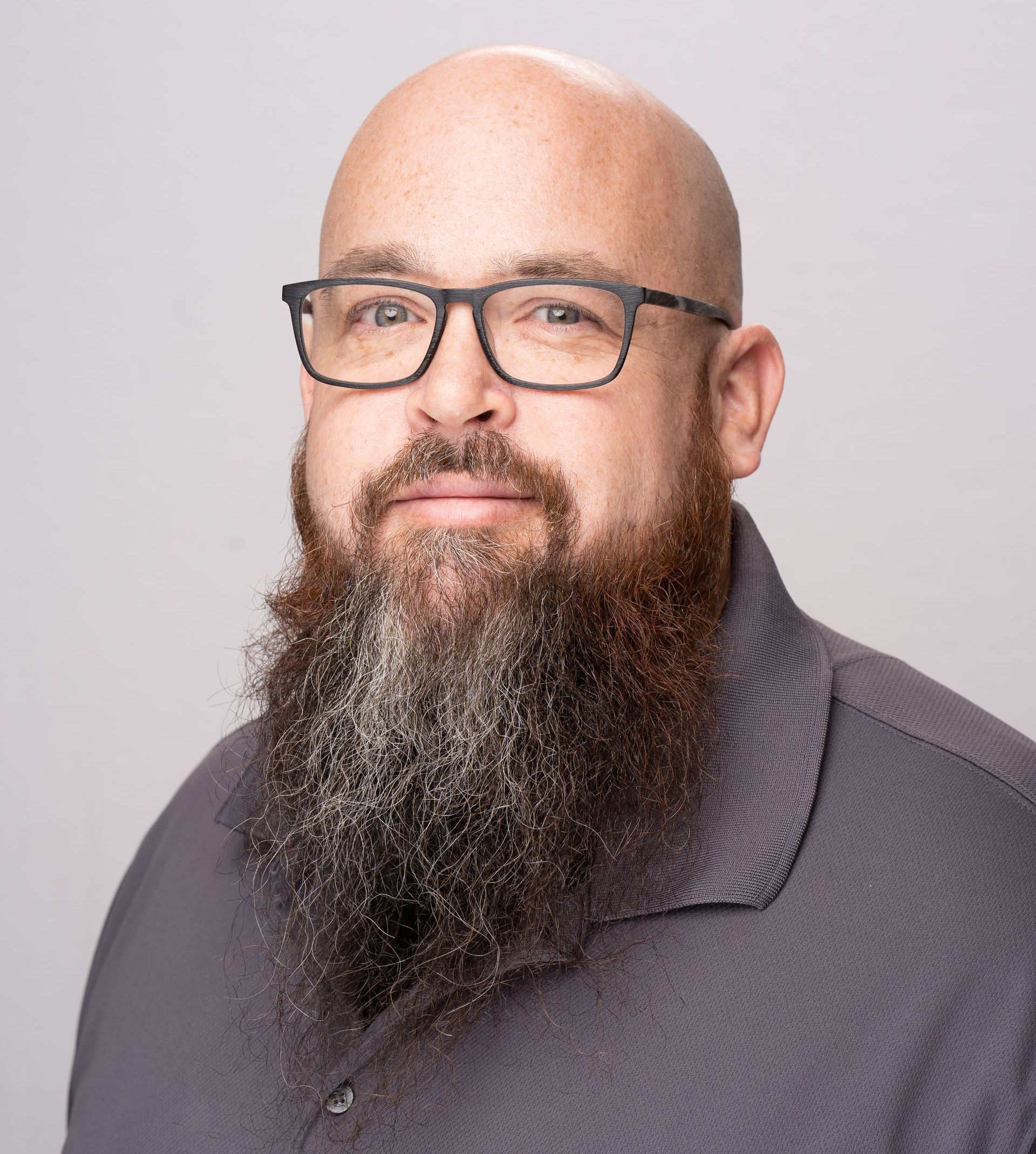 A bald man with a beard and glasses is wearing a black shirt.