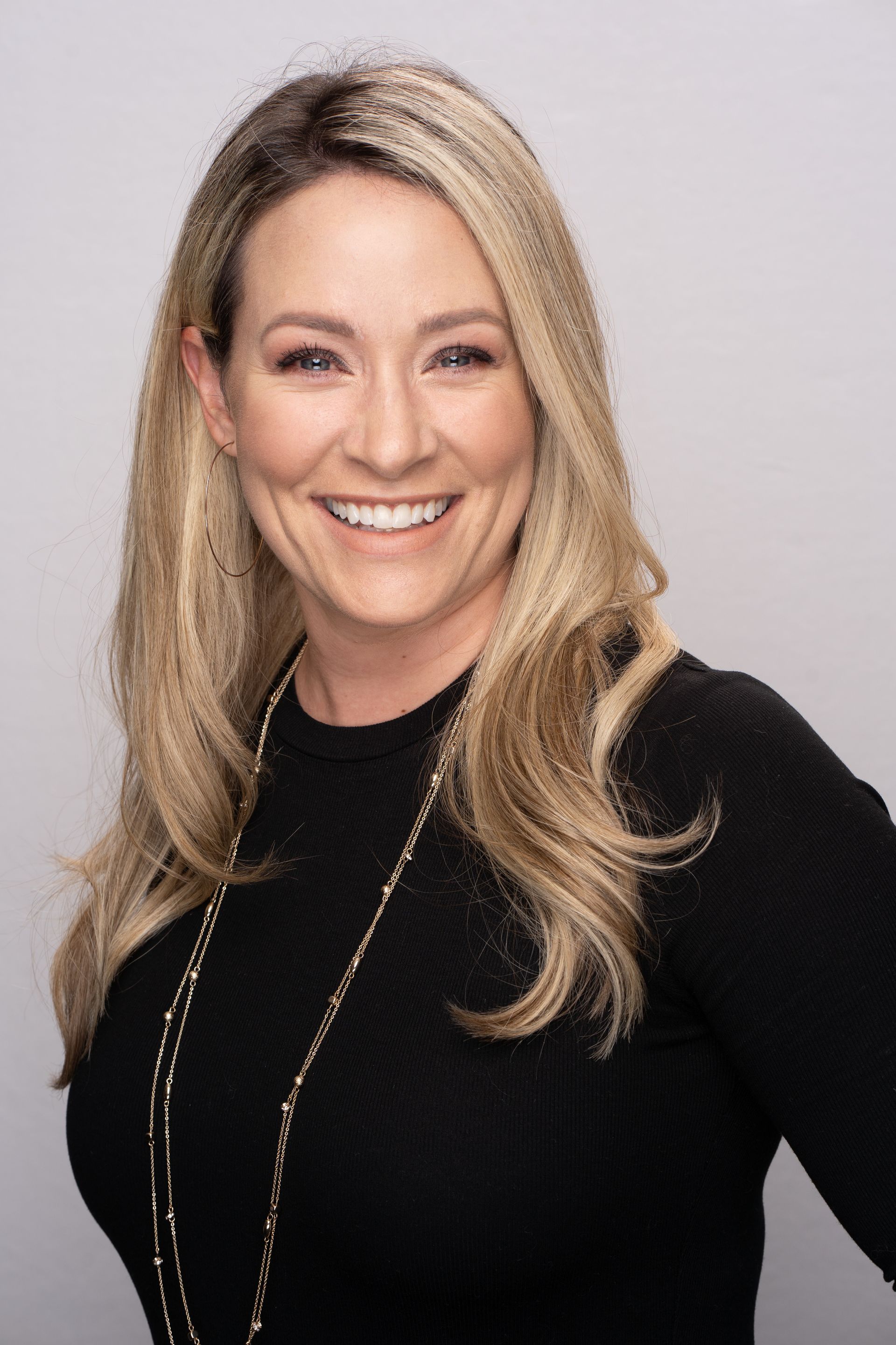 A woman with long blonde hair is smiling and wearing a black shirt.