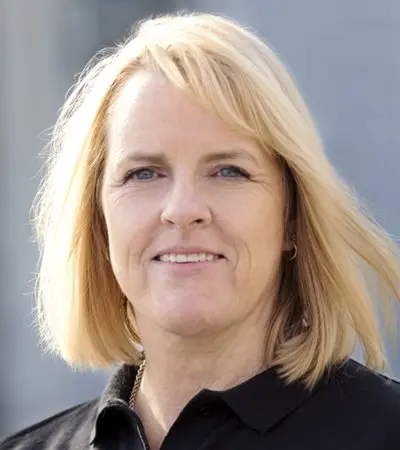 A woman with blonde hair is wearing a black shirt and smiling.