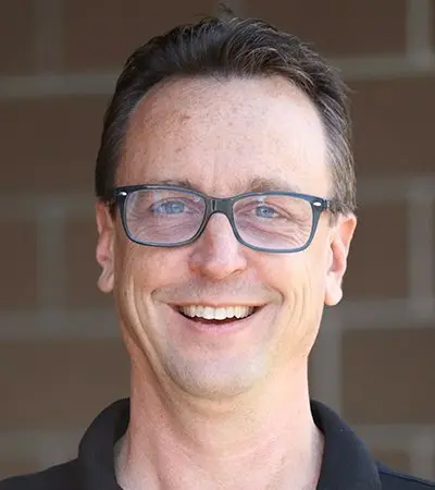 A man wearing glasses and a black shirt is smiling for the camera.