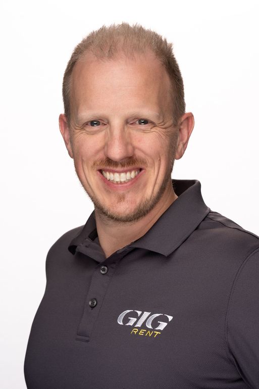 A man in a gray shirt is smiling for the camera.