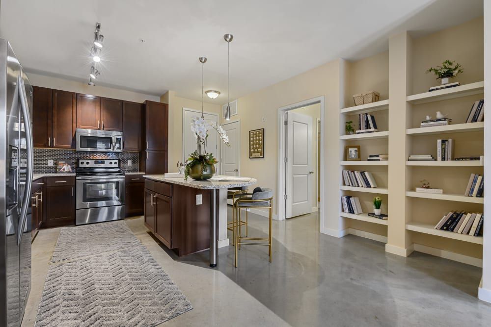 Apartment kitchen with stainless steel appliances, wooden cabinets, and a large island with an open floor plan layout at The 704 in South Lamar Austin, TX.