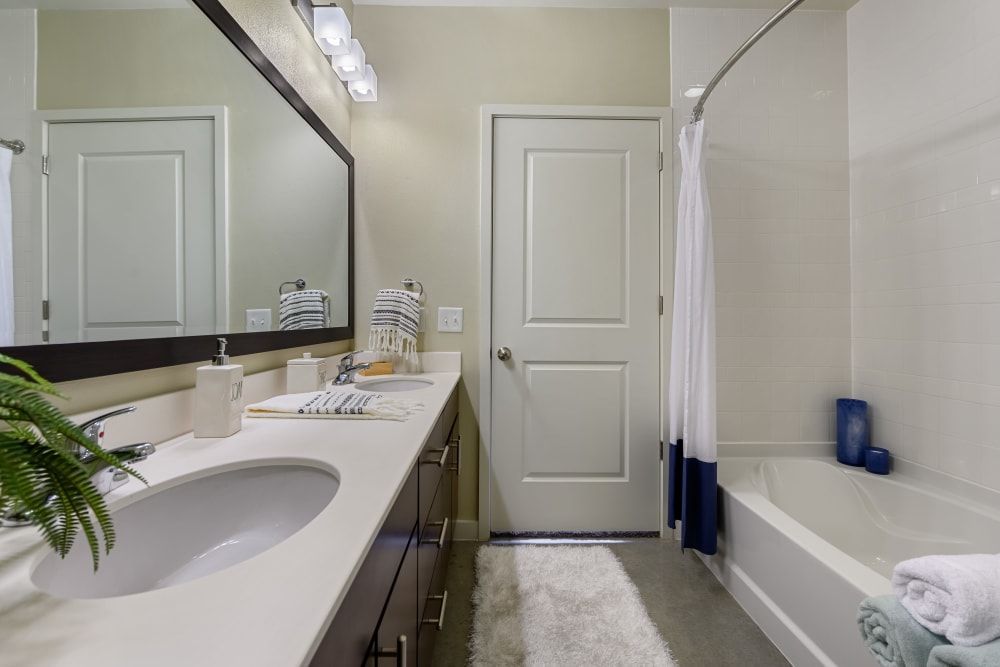 Spacious apartment bathroom with a sink, tub, and mirror at The 704 in Austin TX.