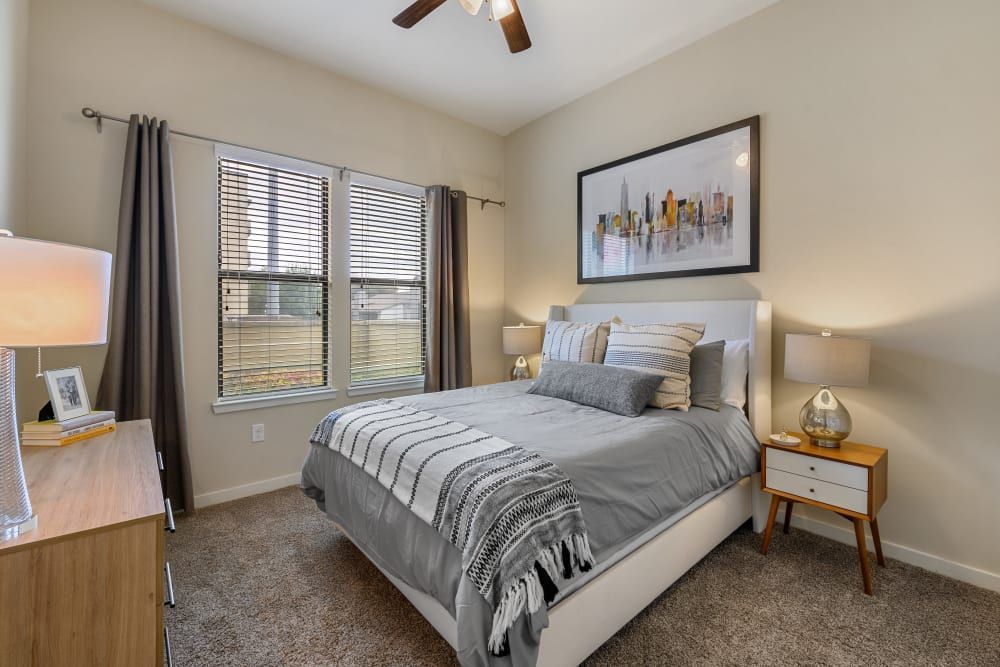 Apartment bedroom with a bed, dresser, nightstand, and ceiling fan at The 704 in South Lamar Austin, TX.