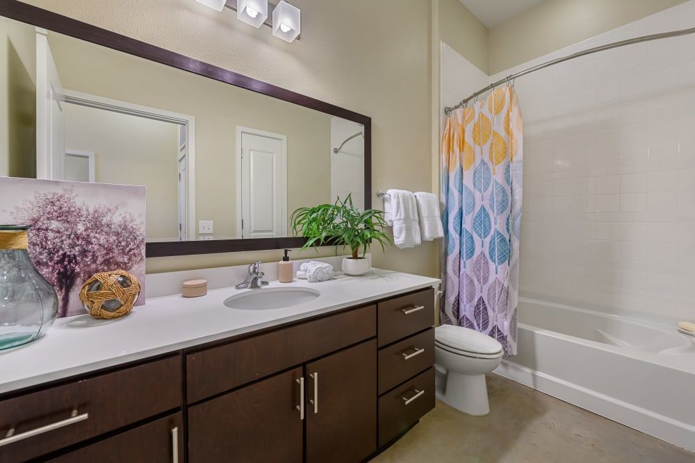Apartment bathroom with a sink, toilet, bathtub and mirror at The 704 in Austin TX.