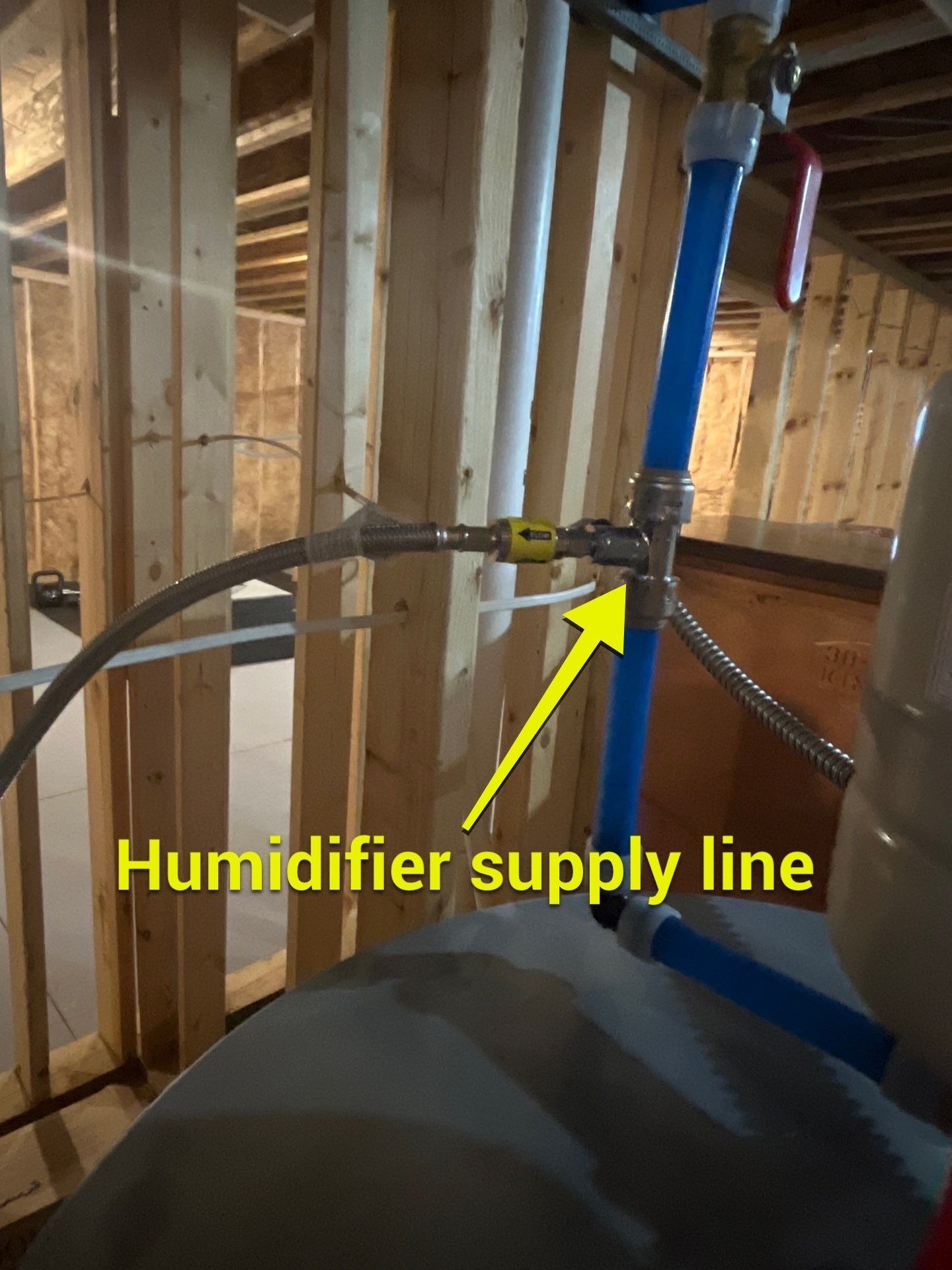 A yellow arrow points to a humidifier supply line connected to blue PEX piping in an unfinished basement.