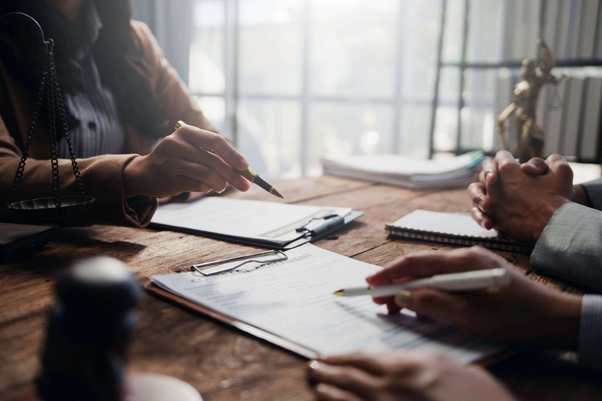 People review legal documents on a wooden desk, with a scale of justice and gavel nearby in a professional office.