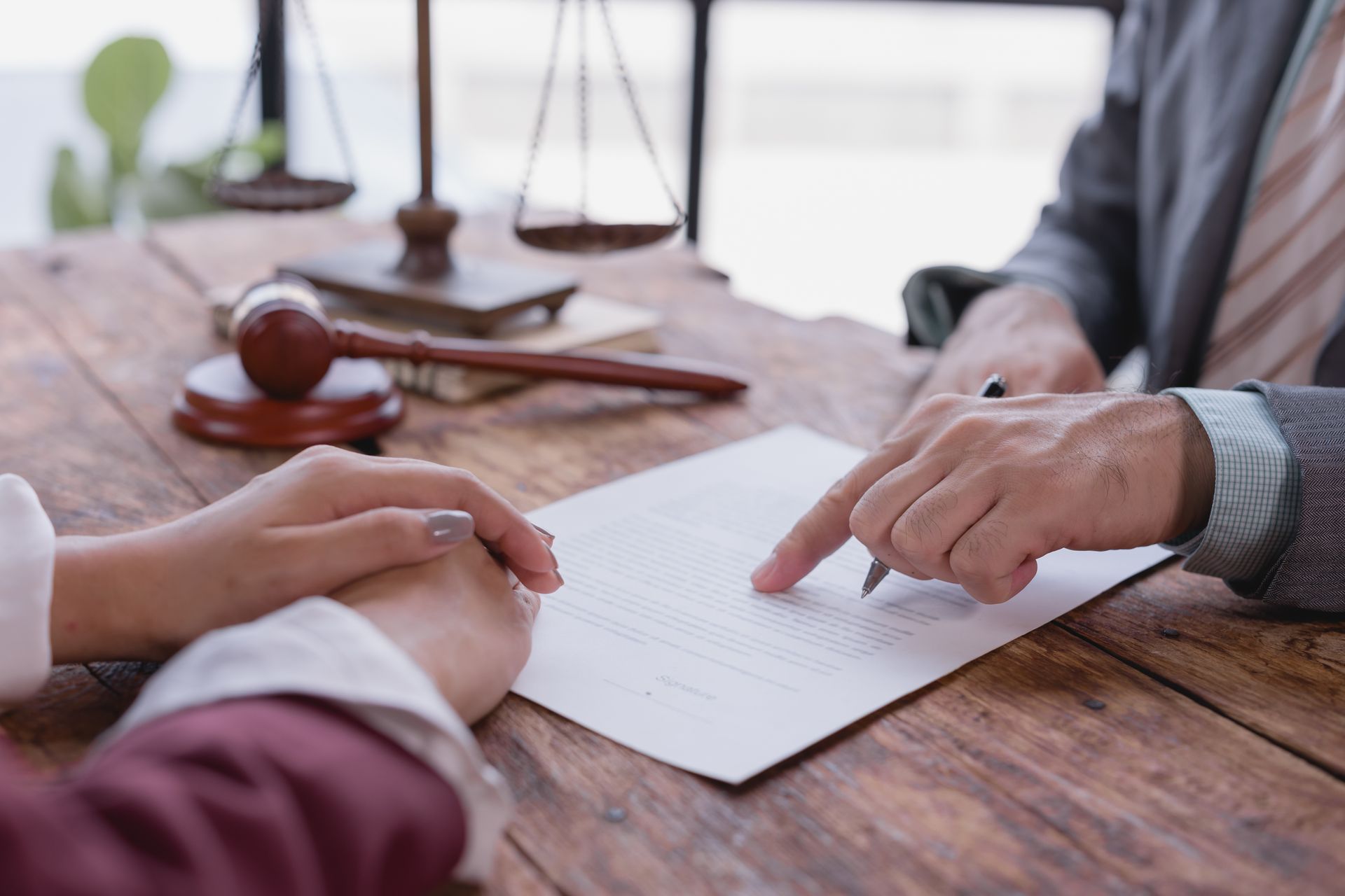 A person pointing at a document on a wooden desk with a judge's gavel and scales of justice in the background.